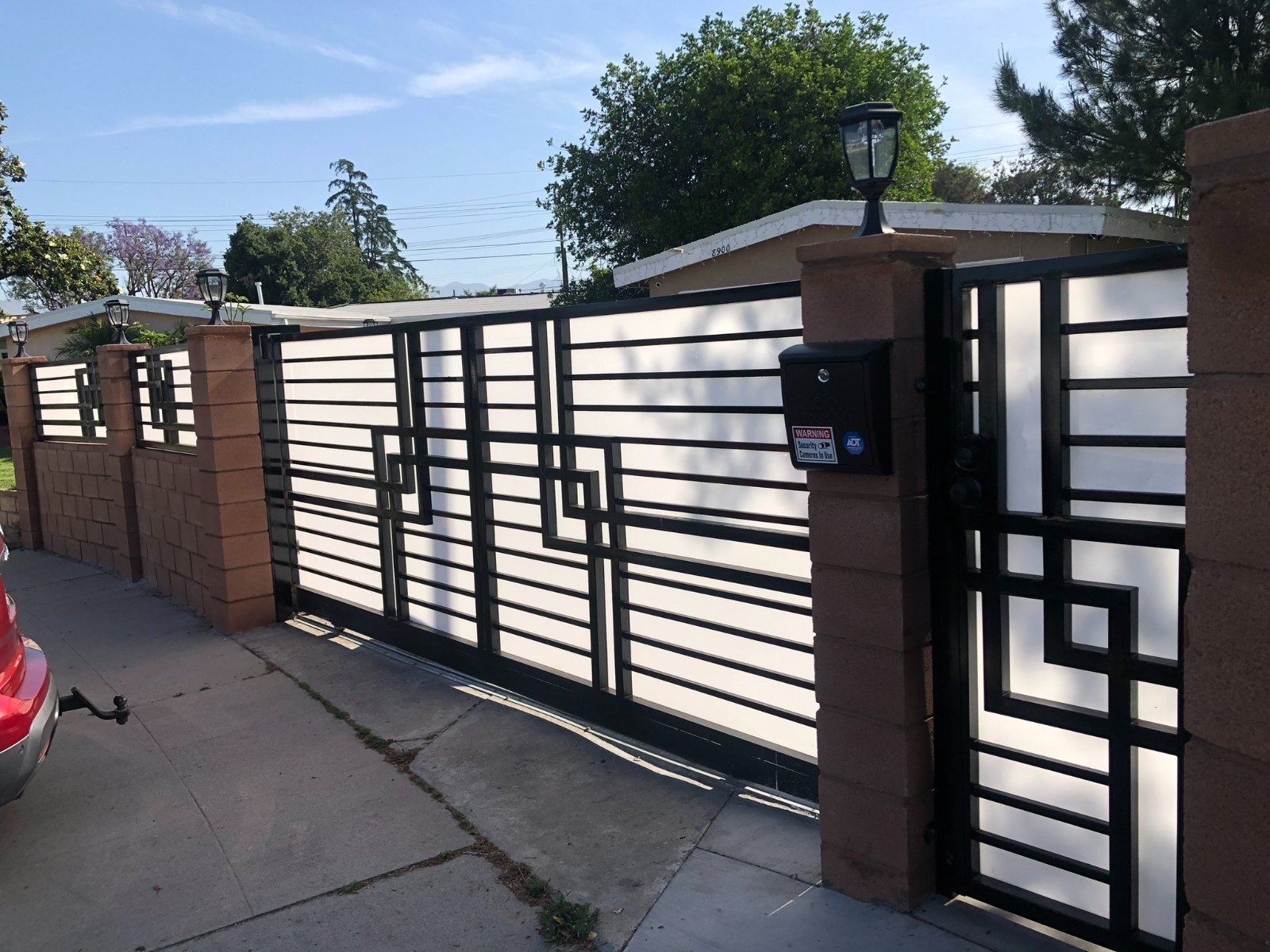 Modern geometric steel driveway gate and matching pedestrian gate between brick pillars in Canoga Park