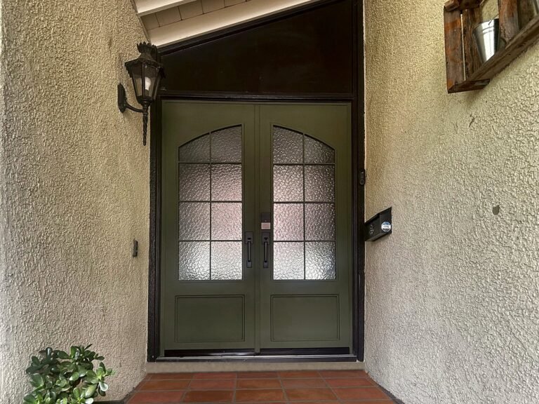 Green iron double entry door with arched textured-glass windows under a covered entry