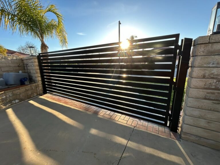 Black horizontal slat steel sliding driveway gate beside a block wall in Stevenson Ranch