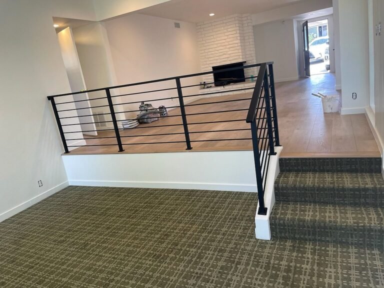 Black horizontal bar iron railing along a raised floor edge and stairs in a living room