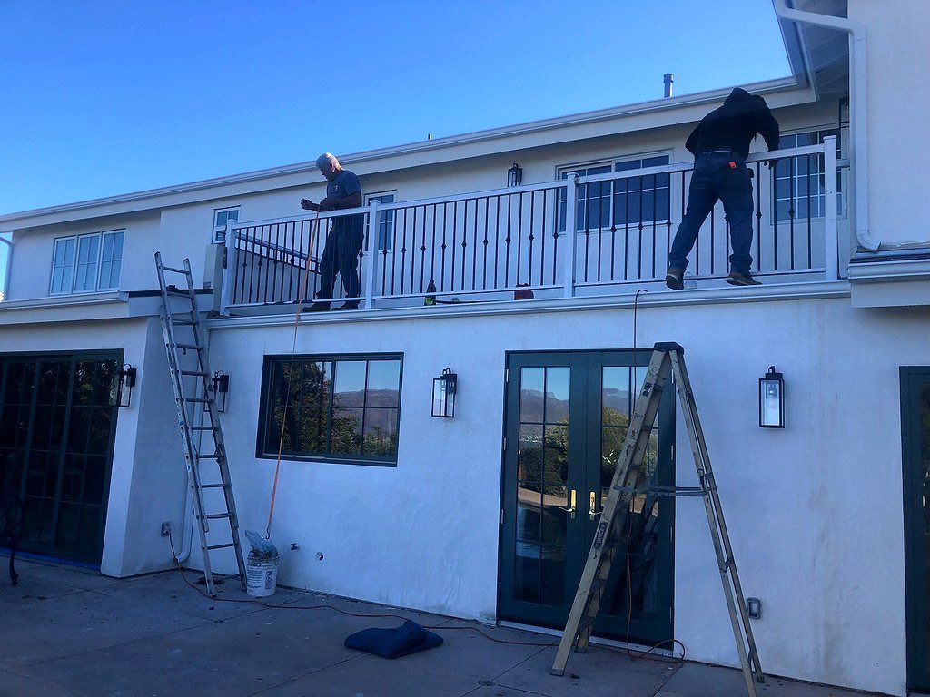 Crew installing a white iron balcony railing on a second-story deck