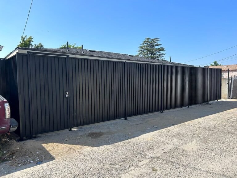 Long black solid steel privacy fence along a driveway