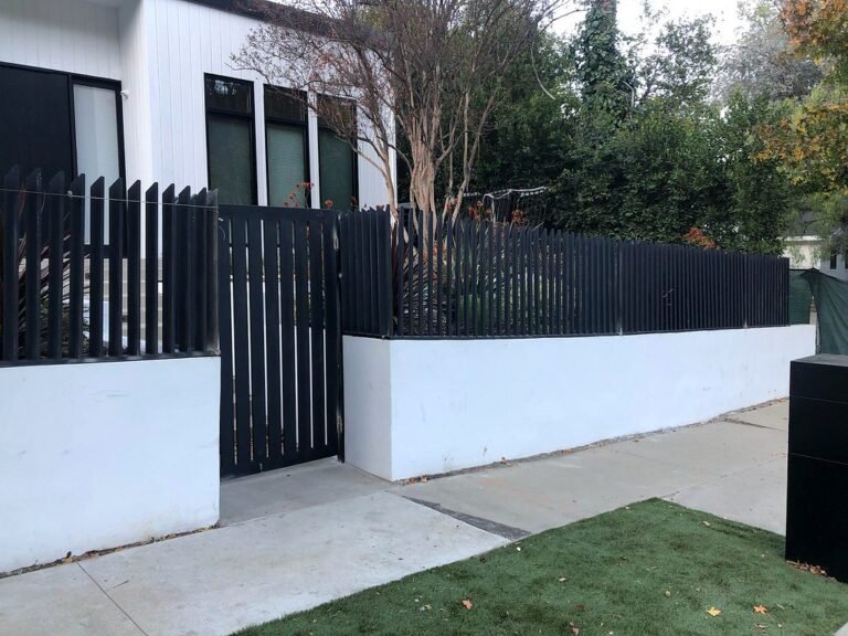 Modern black iron picket fence and gate on a white stucco wall