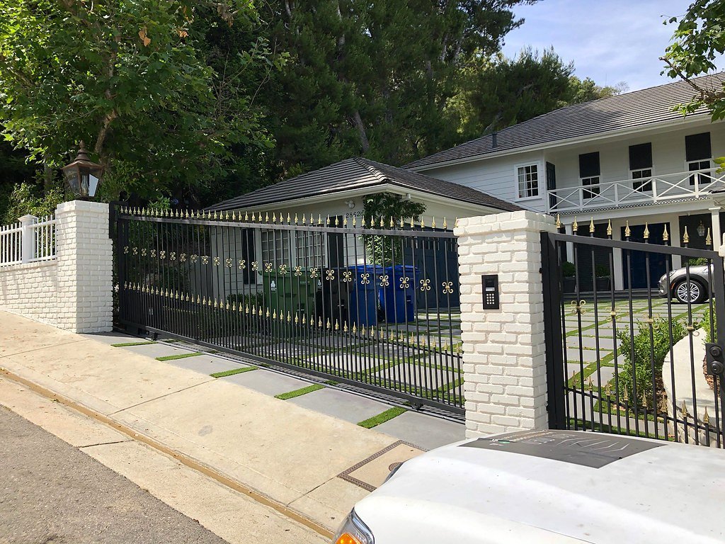 Black iron driveway gate between white brick pillars
