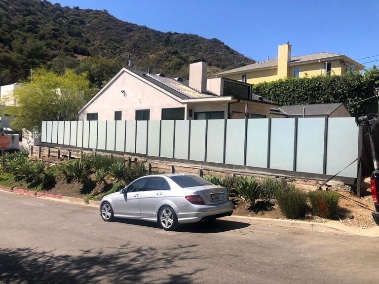 Frosted glass panel fence with black iron posts along a hillside home