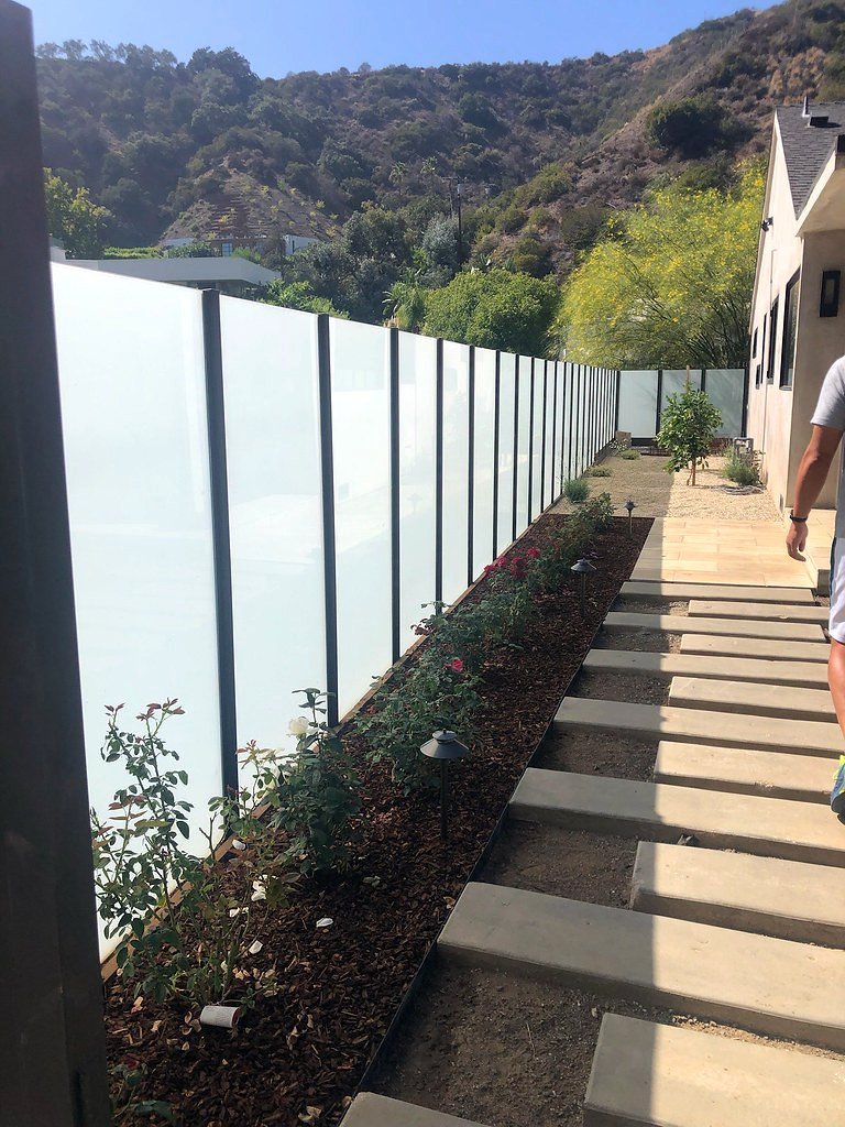 Frosted glass panel fence with iron posts beside hillside garden steps