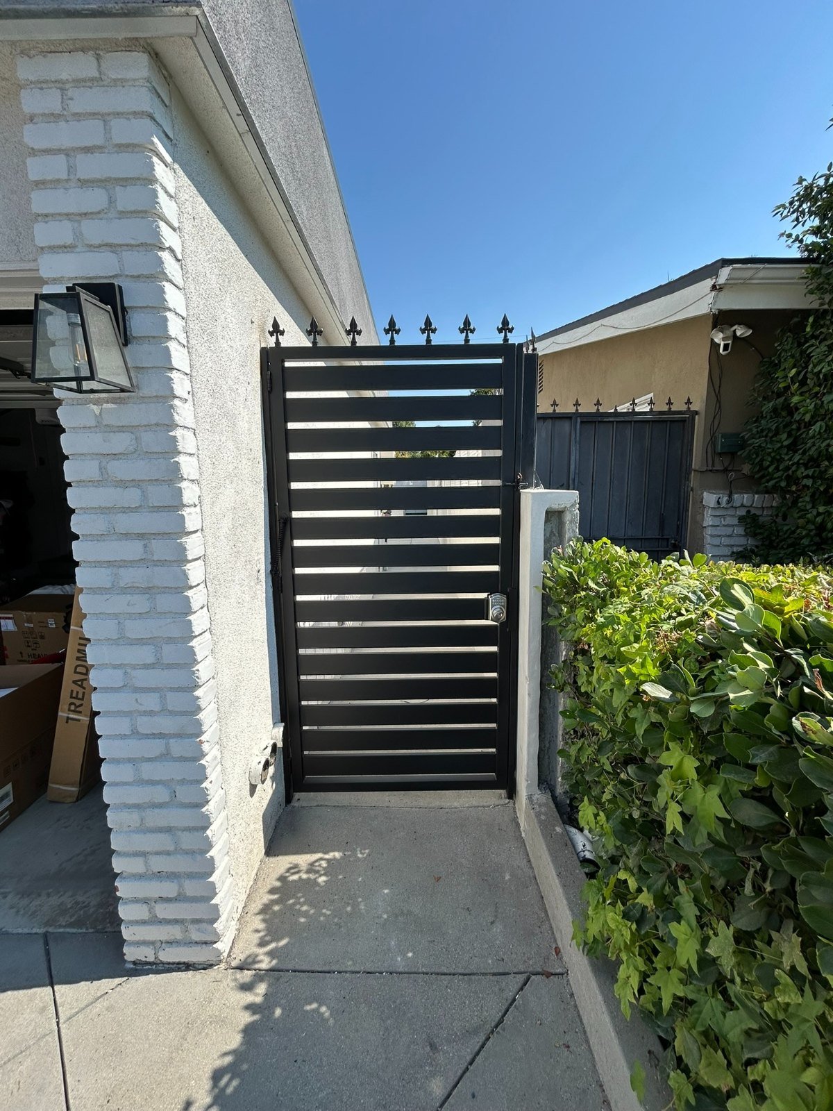 Narrow black steel picket side gate beside a white brick wall in Sierra Madre