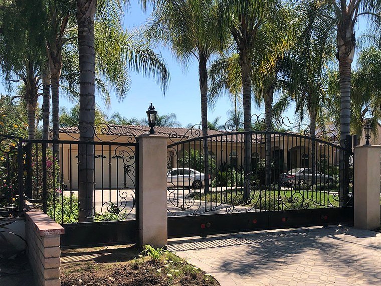 Ornamental wrought iron driveway gate and fence with stucco pillars and palm trees
