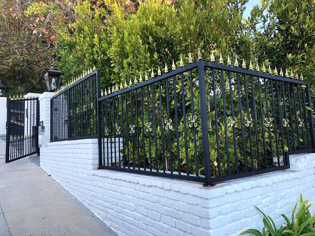 Black wrought iron fence with gold spear tops and fleur-de-lis accents on a white brick wall