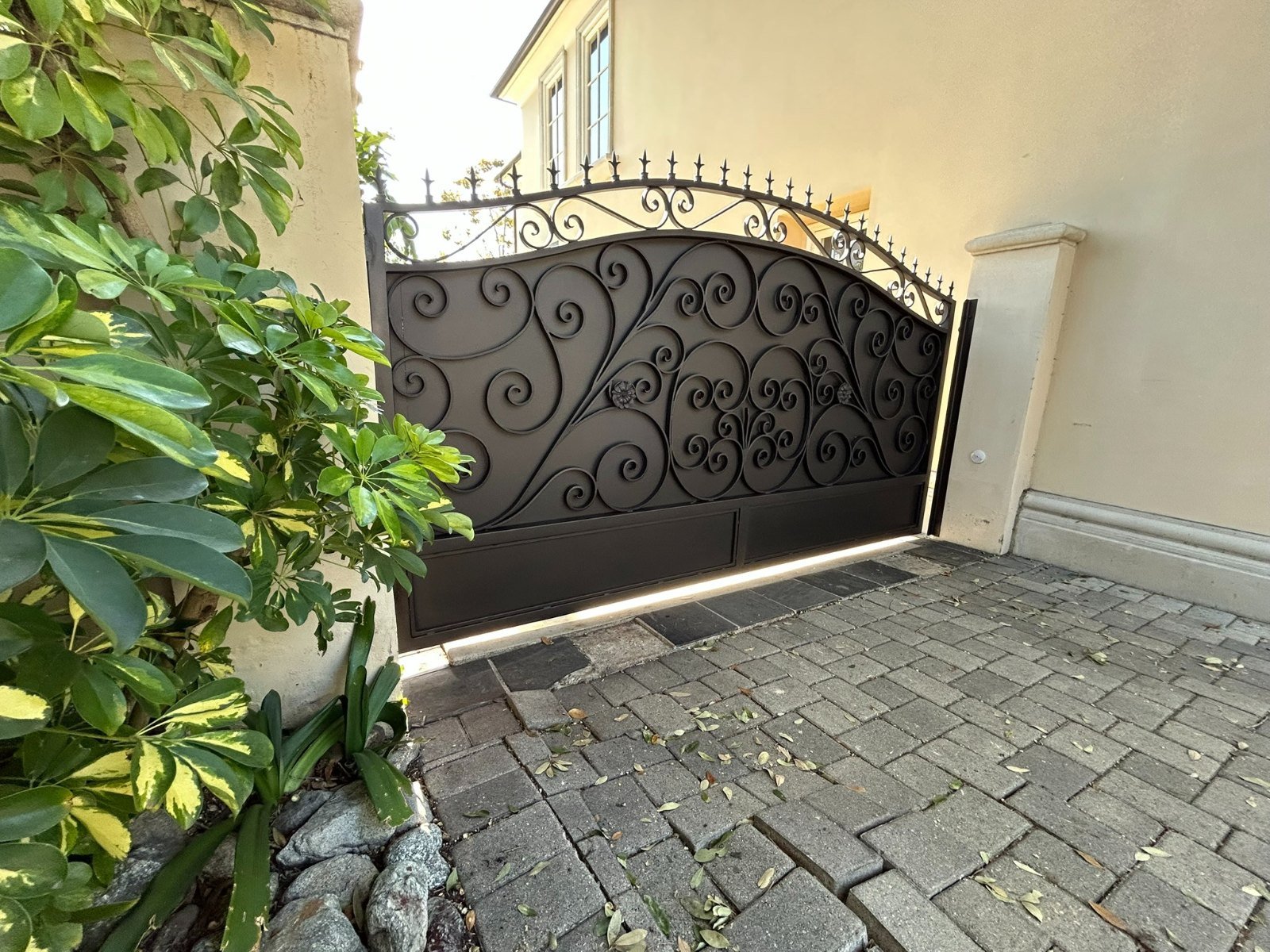 Solid steel driveway gate with an arched wrought iron scroll top on a paver driveway in San Marino