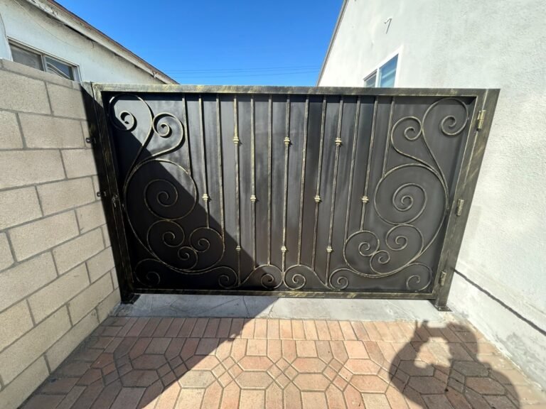 Solid black steel gate with scrollwork accents between block walls in Covina