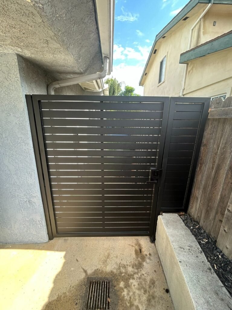 Black horizontal slat steel side gate between stucco walls in Montrose