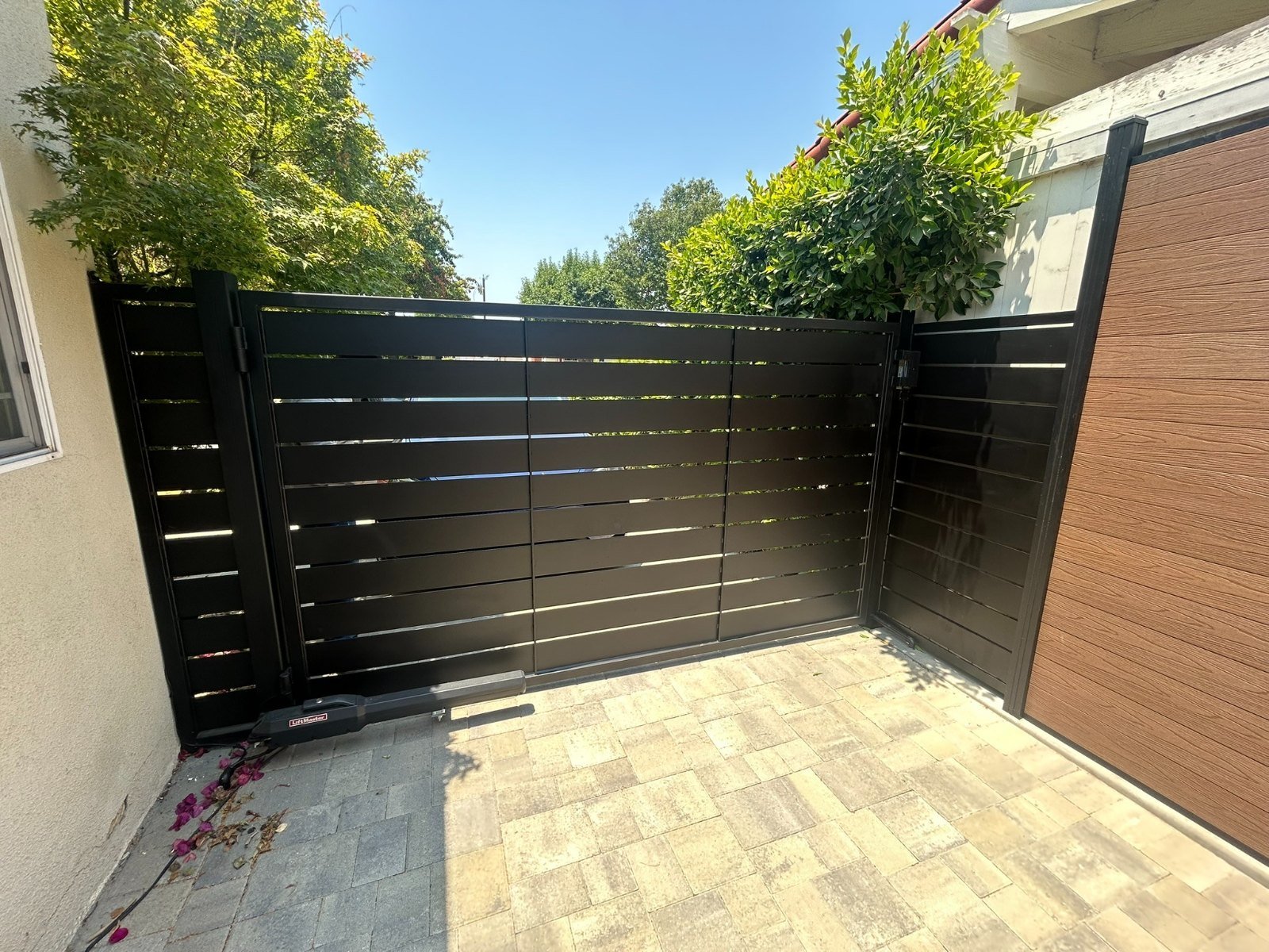 Wide black horizontal slat steel driveway gate on a paver driveway in Redondo Beach